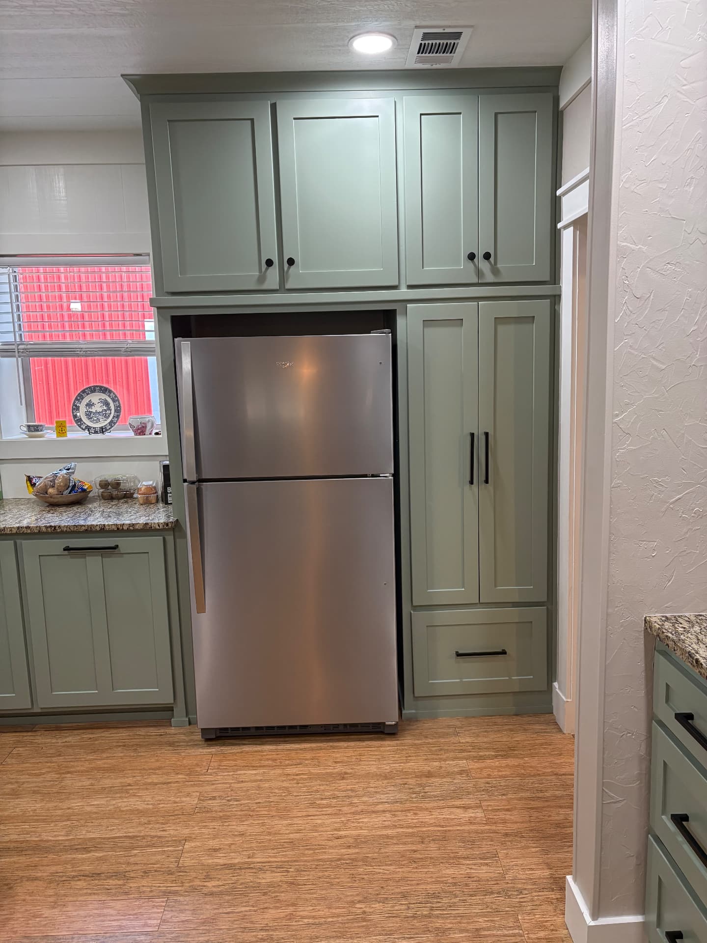 Finished refrigerator wall with sage-green custom cabinetry